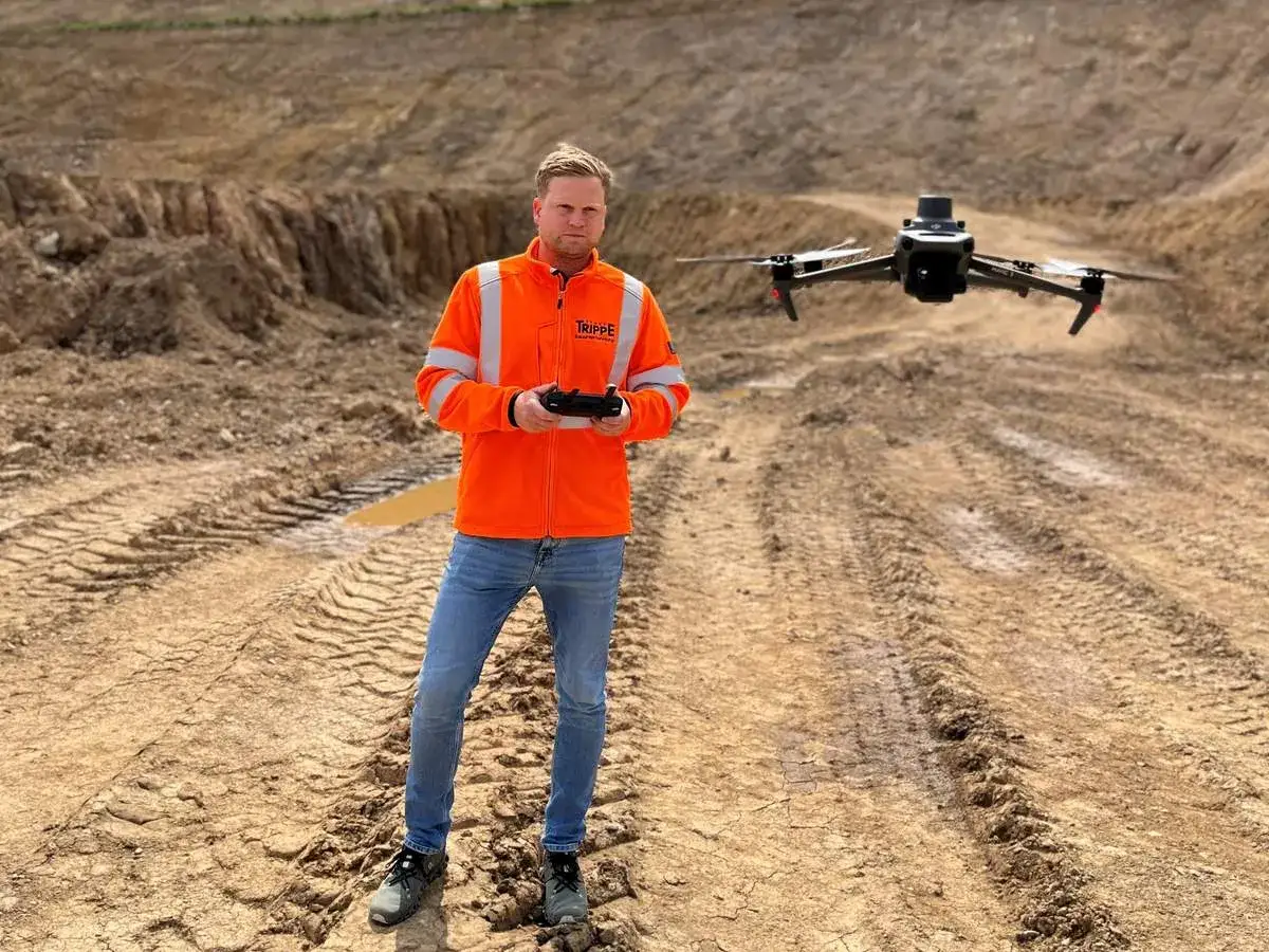 Mann in Warnweste steuert Drohne für präzise **Drohnen Maps** auf Baustelle.