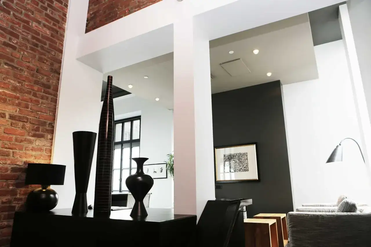 Vasi neri e una lampada per abbellire una colonna in un loft con mattoni a vista e arredi moderni.