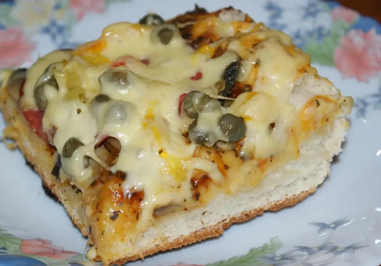 Pyszna pizza na grubym cieście, obficie posypana serem i kaparami, kusi apetycznym wyglądem.