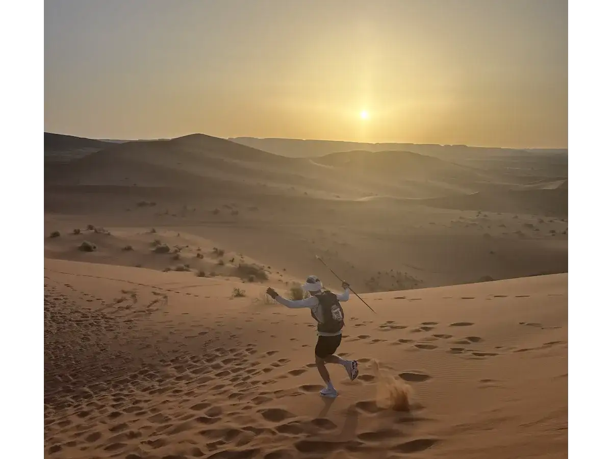 L&auml;ufer k&auml;mpft sich durch die D&uuml;nen des Marathon des Sables. Die Sonne geht unter und wirft lange Schatten.