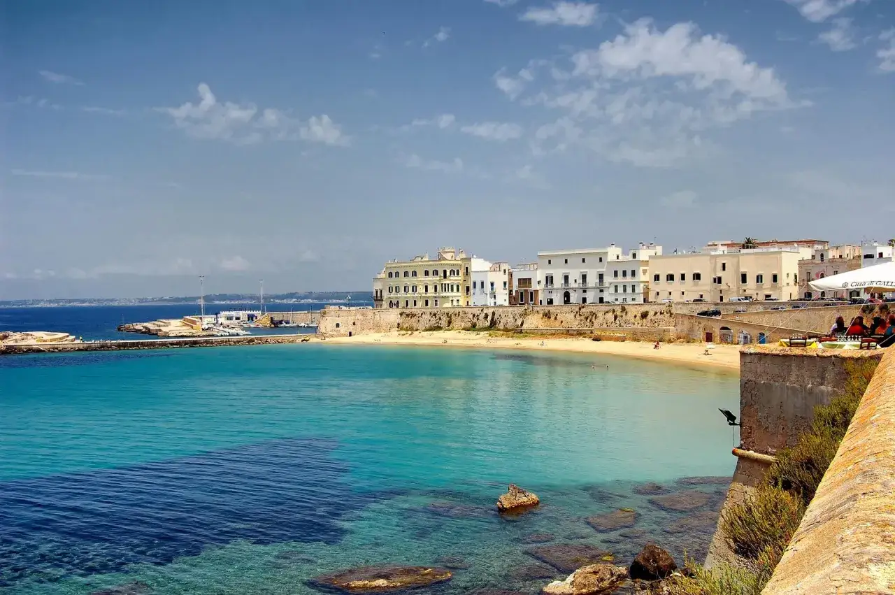 La splendida **Gallipoli citt&agrave;** con le sue case bianche affacciate sul mare turchese. Una baia tranquilla con una spiaggia dorata e rocce affioranti.