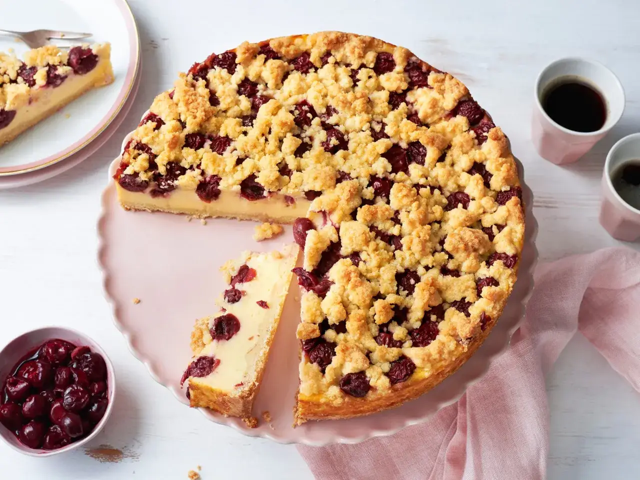 Ein saftiger Kirschkuchen mit Puddingfüllung und knuspriger Streuseldecke, serviert auf einer rosa Tortenplatte.