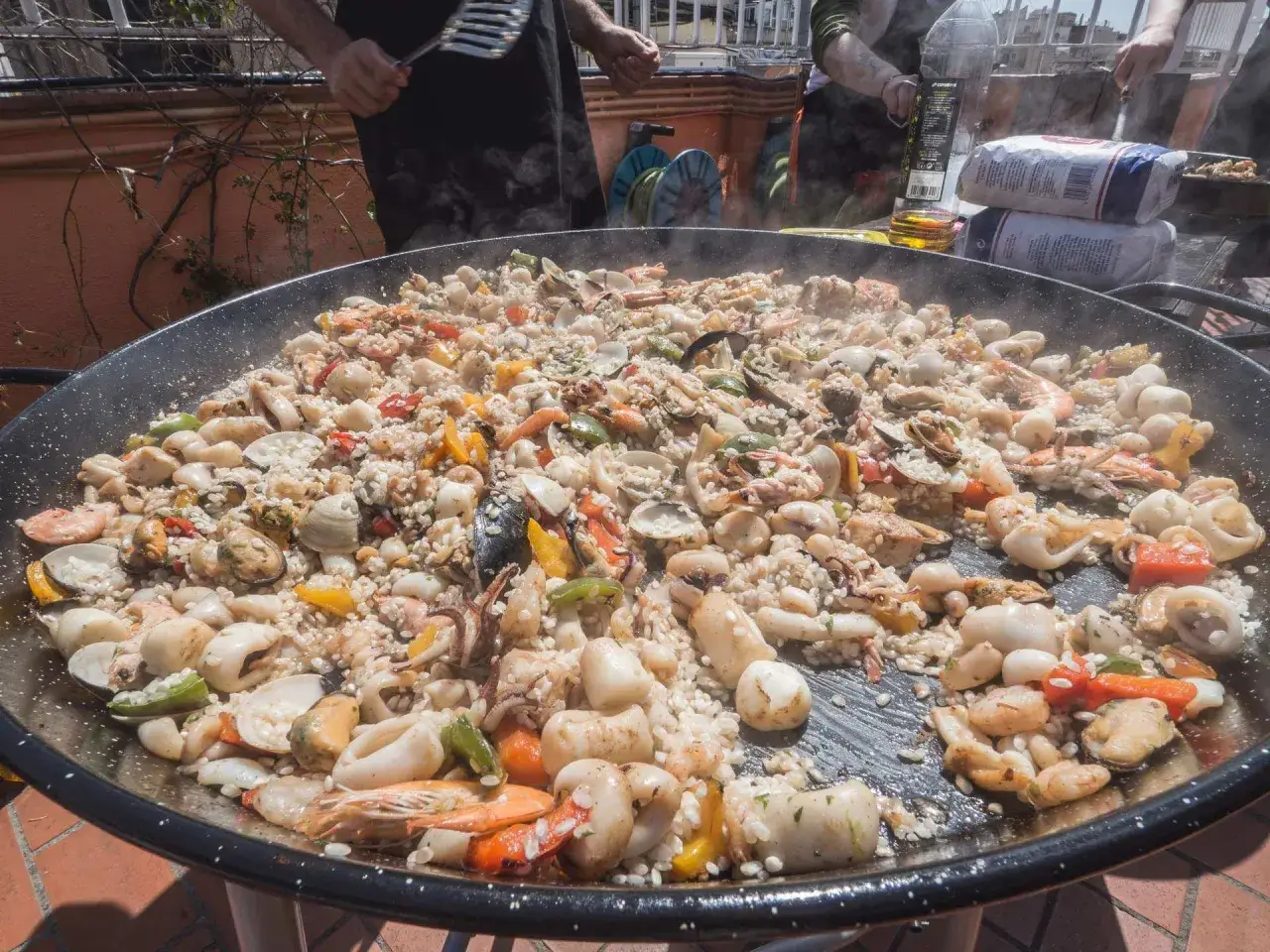 Ogromna patelnia z parującą paellą pełną owoców morza i ryżu, przygotowywana na świeżym powietrzu. To musi być najlepsza paella w Barcelonie!