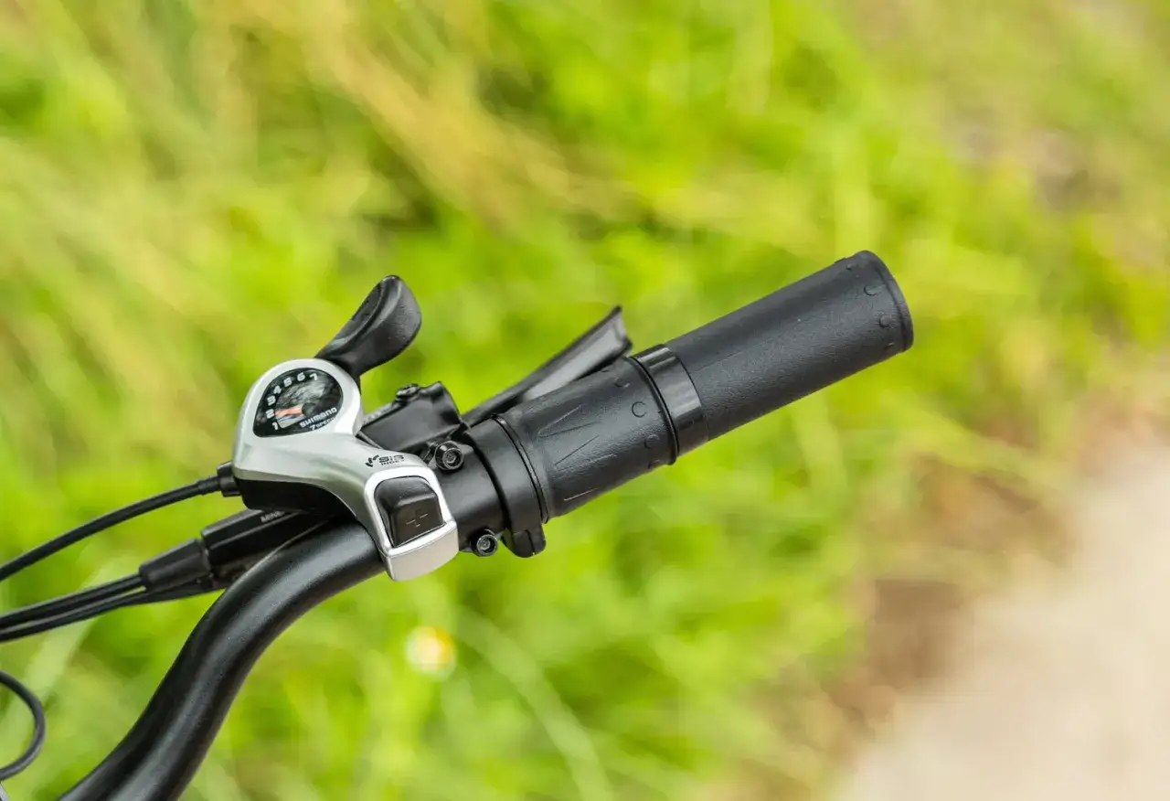 Manetka przerzutek Shimano na kierownicy roweru, gotowa do zmiany biegów podczas jazdy po zielonym tle.