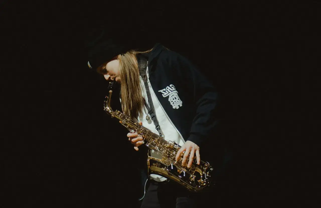 Jeune musicien concentr&eacute; jouant d'un instrument de musique en s, un saxophone dor&eacute;, sur fond noir.