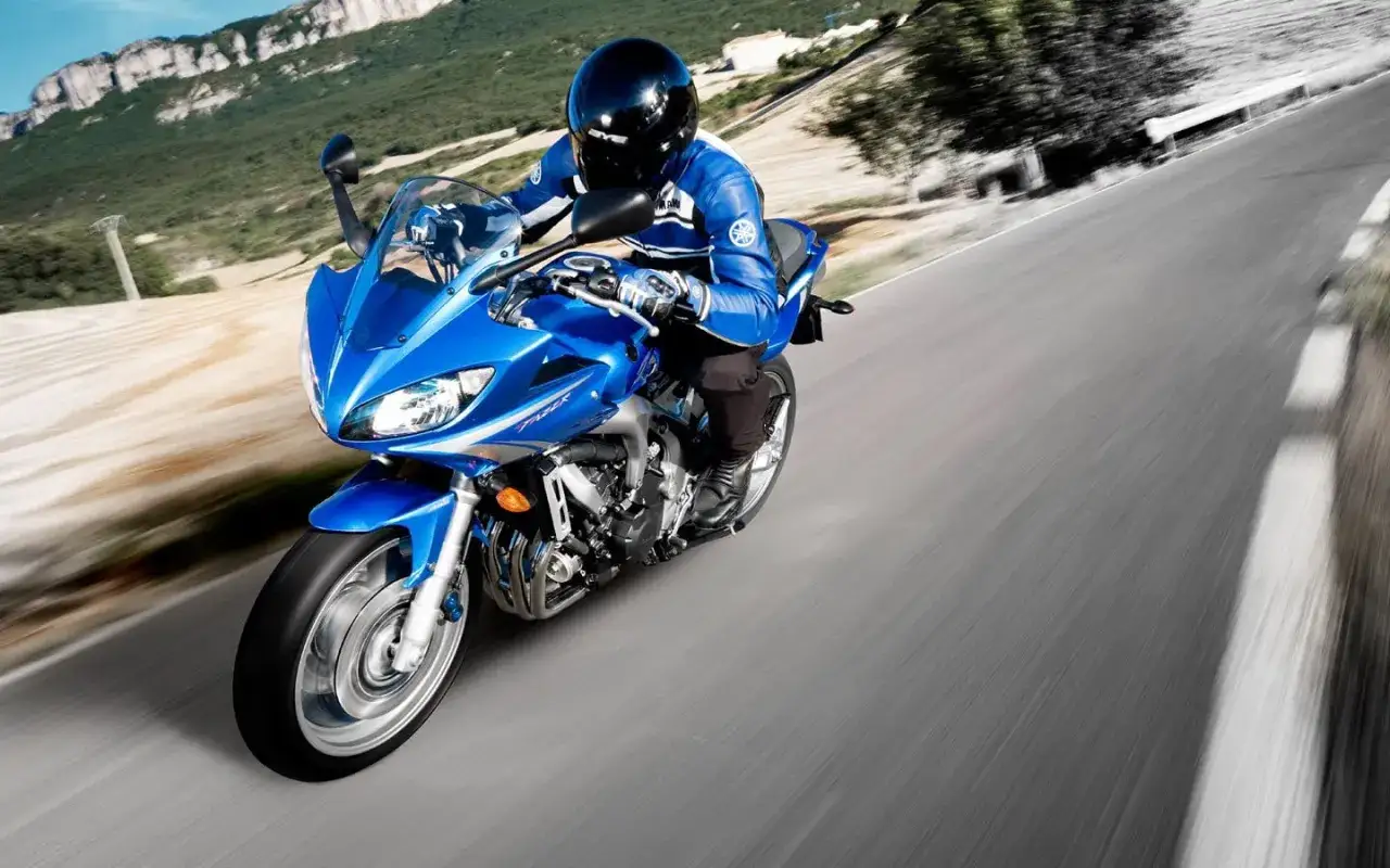 Błękitny motocykl Yamaha FZ6 z kierowcą w niebieskim kombinezonie pędzi po krętej drodze wśród gór.