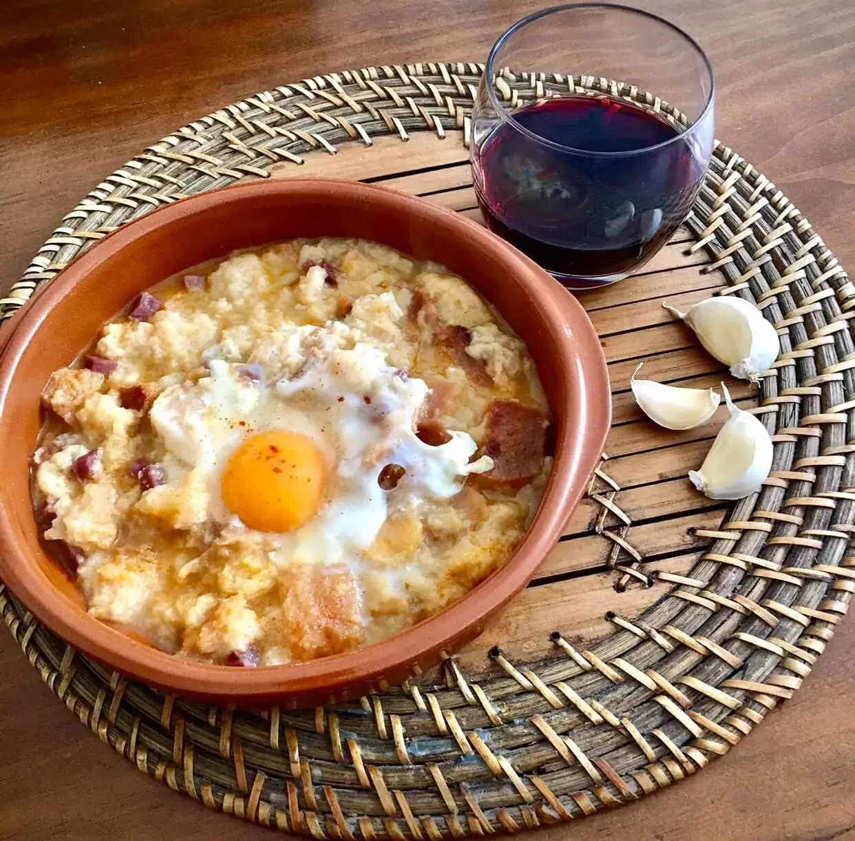 Sopa de ajo servida en cuenco de barro con copa de vino tinto