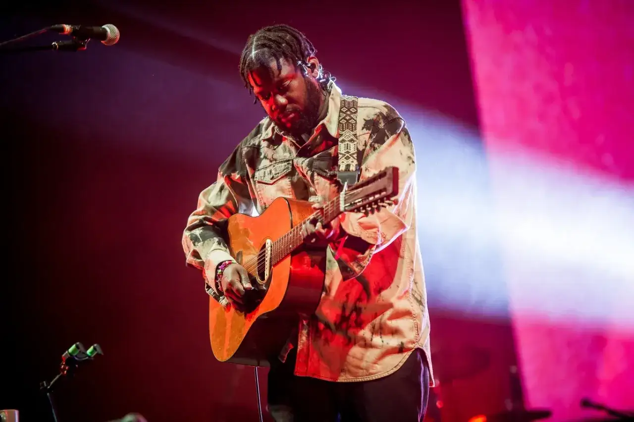 Michael Kiwanuka na koncercie, grając na gitarze.