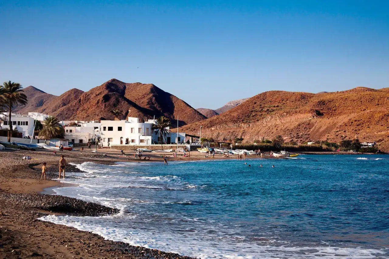 Gente disfrutando en la playa Las Negras, con casas blancas y montañas rojizas de fondo.