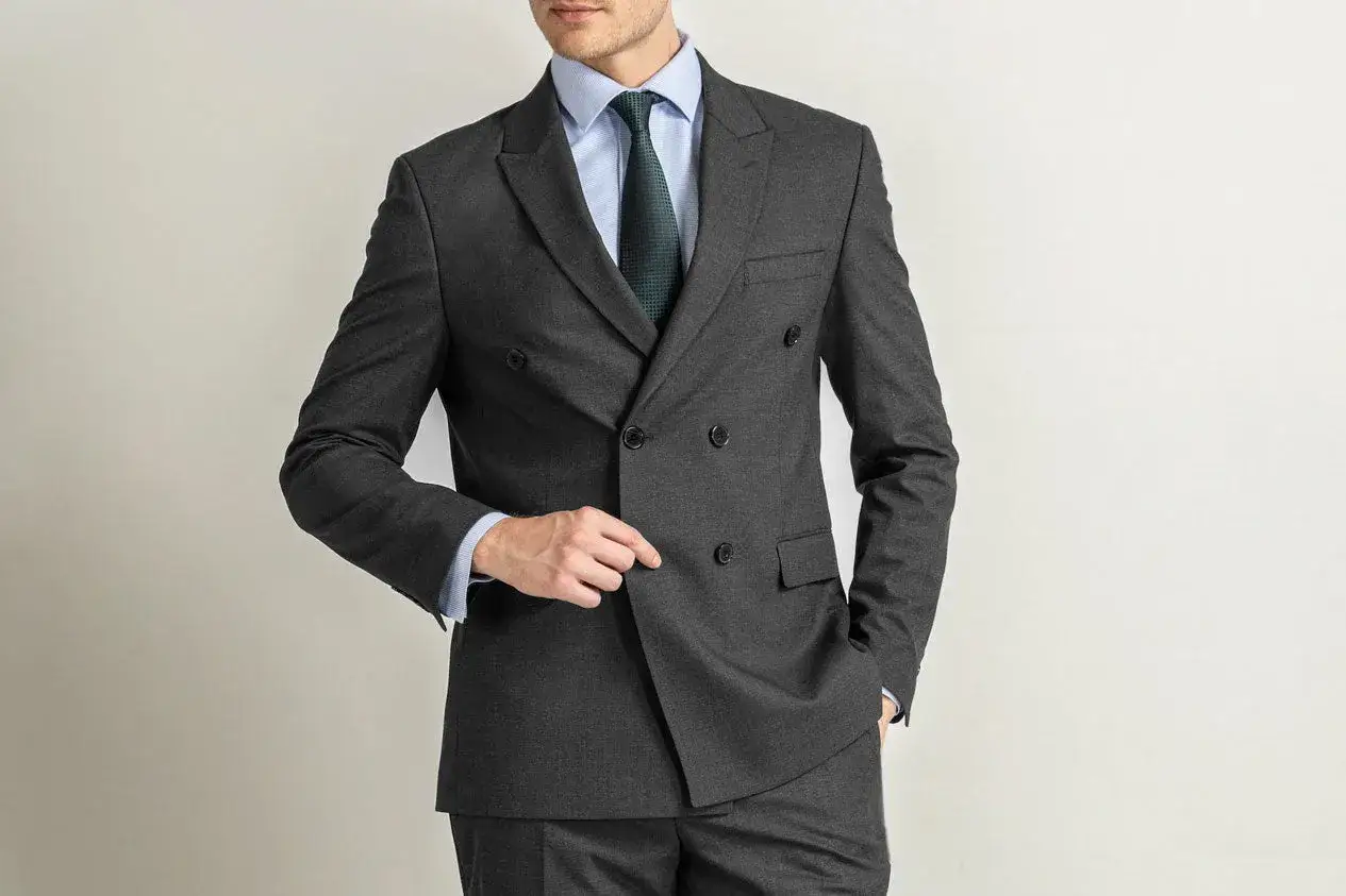 A man models a sharp charcoal suit, showcasing classic double-breasted styling. This charcoal suit combination is perfect for any formal occasion.