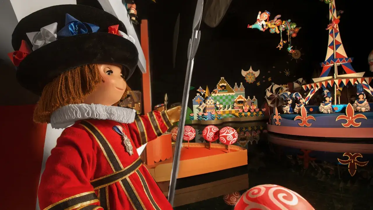 Muñeco con traje rojo y sombrero, sosteniendo una lanza, frente a un escenario de 