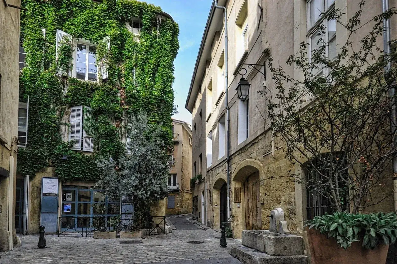 Calle empedrada con casas antiguas. Una fachada está cubierta de hiedra. Me pregunto si esta casa sin escrituras que he heredado se parecerá a esta.