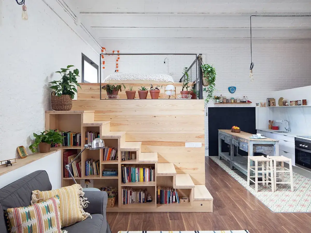 Aménagement mezzanine ouverte avec escalier en bois intégrant des étagères et des rangements. Un lit est visible sur la mezzanine.