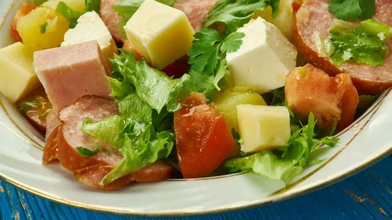 Une id&eacute;e de salade compos&eacute;e : d&eacute;s de jambon, saucisson, fromage, tomates et laitue fra&icirc;che dans une assiette blanche.