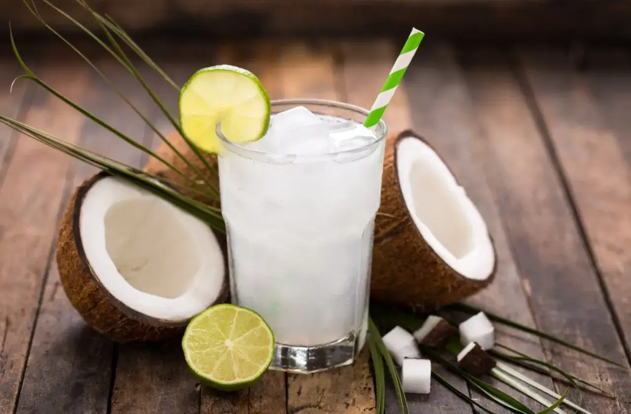 Orzeźwiający drink z wodą kokosową, lodem, limonką i kawałkami kokosa na drewnianym blacie.