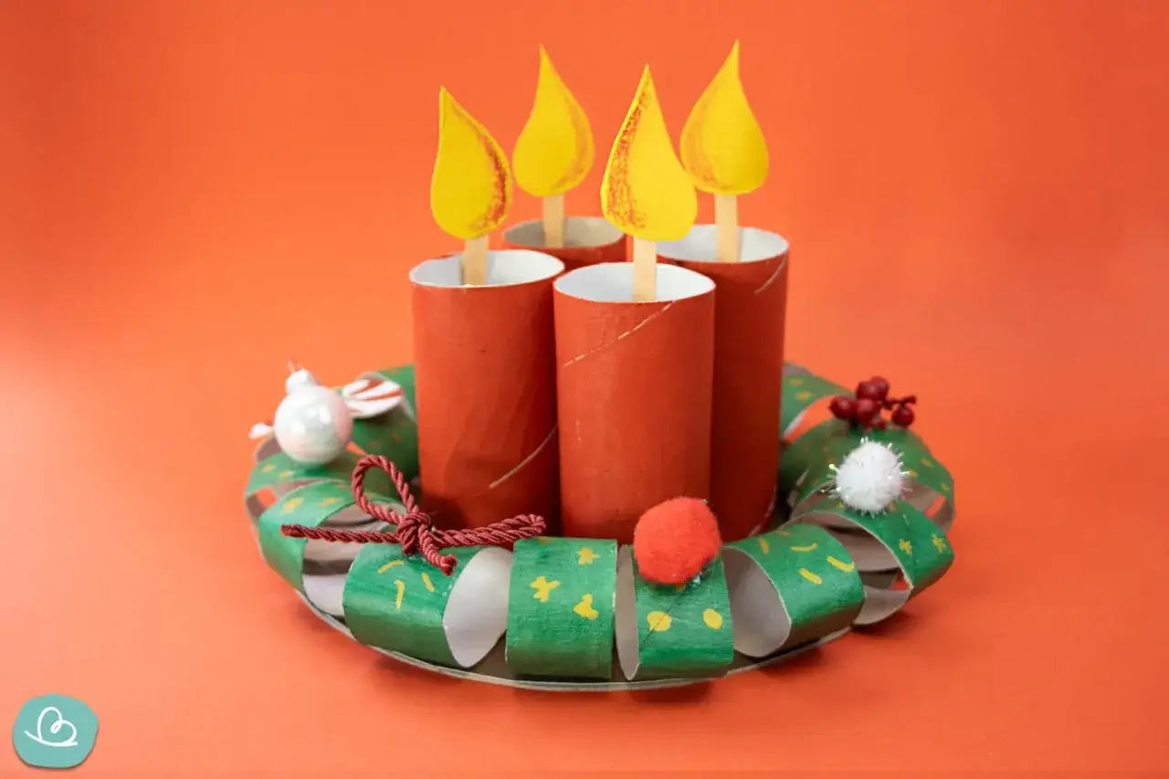 Vier selbstgebastelte Kerzen aus Klopapierrollen auf einem gr&uuml;nen Kranz. Ein tolles Projekt zum **Adventskranz basteln mit Kindern**.
