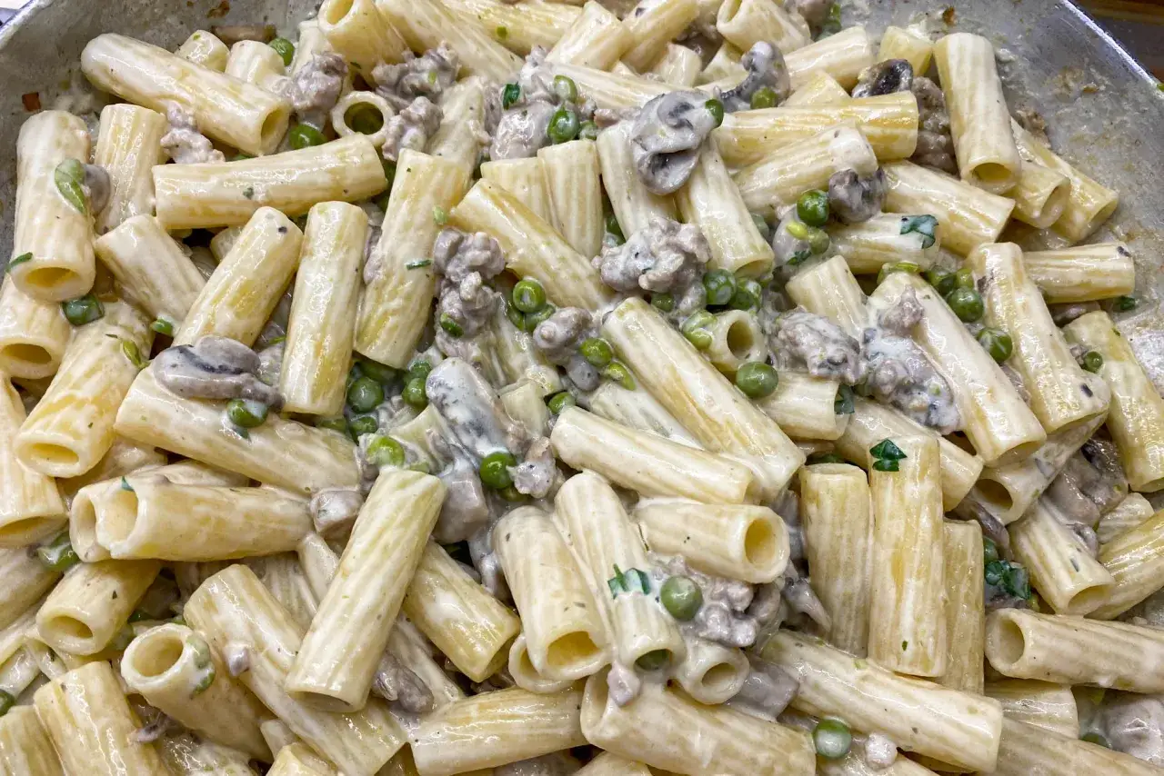 Rigatoni cremosi con piselli, funghi e salsiccia, un invitante piatto di pasta alla boscaiola pronto per essere gustato.