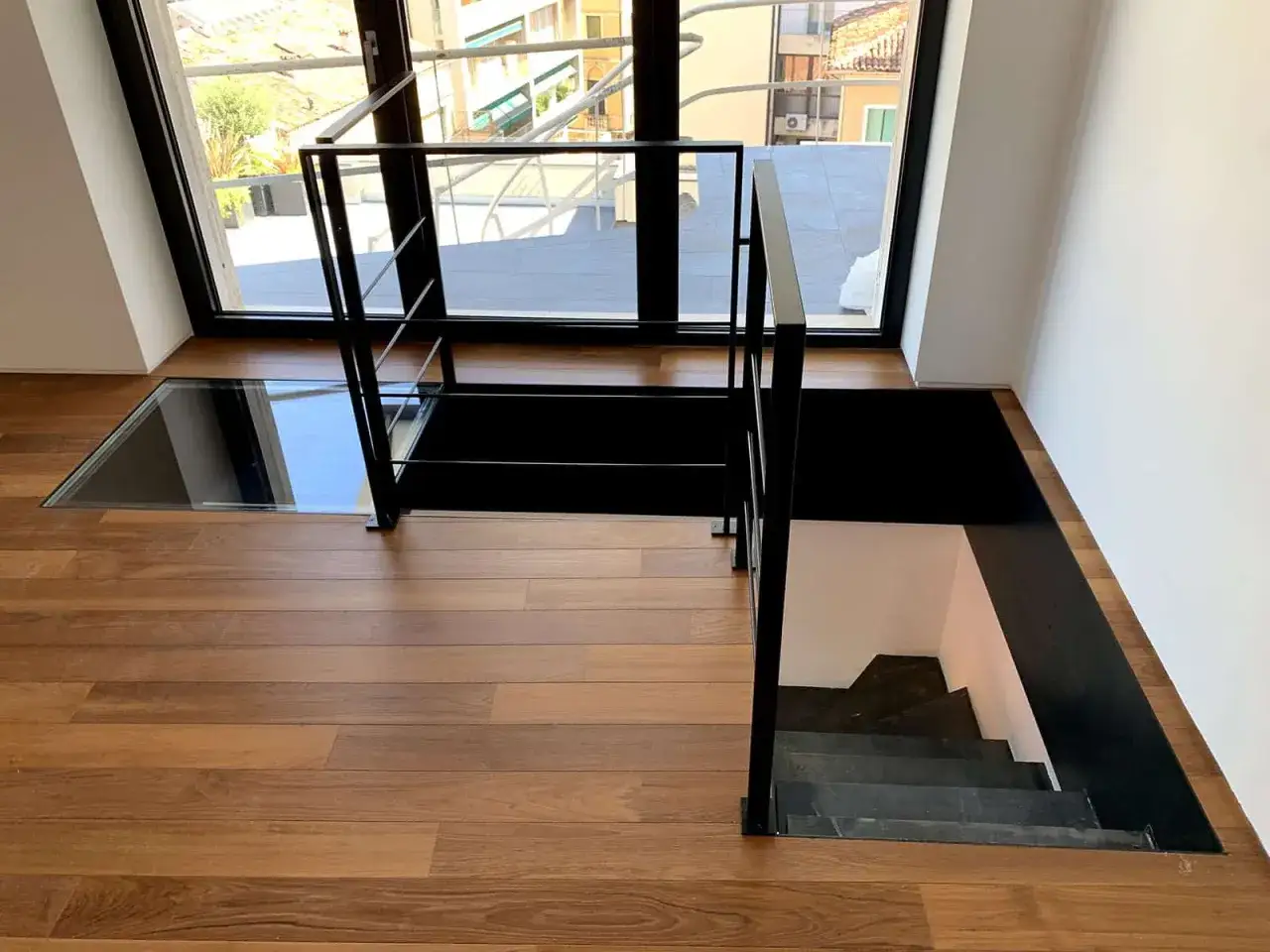 Parapetto scala interna design moderno in metallo nero con gradini a vista e pavimento in legno.