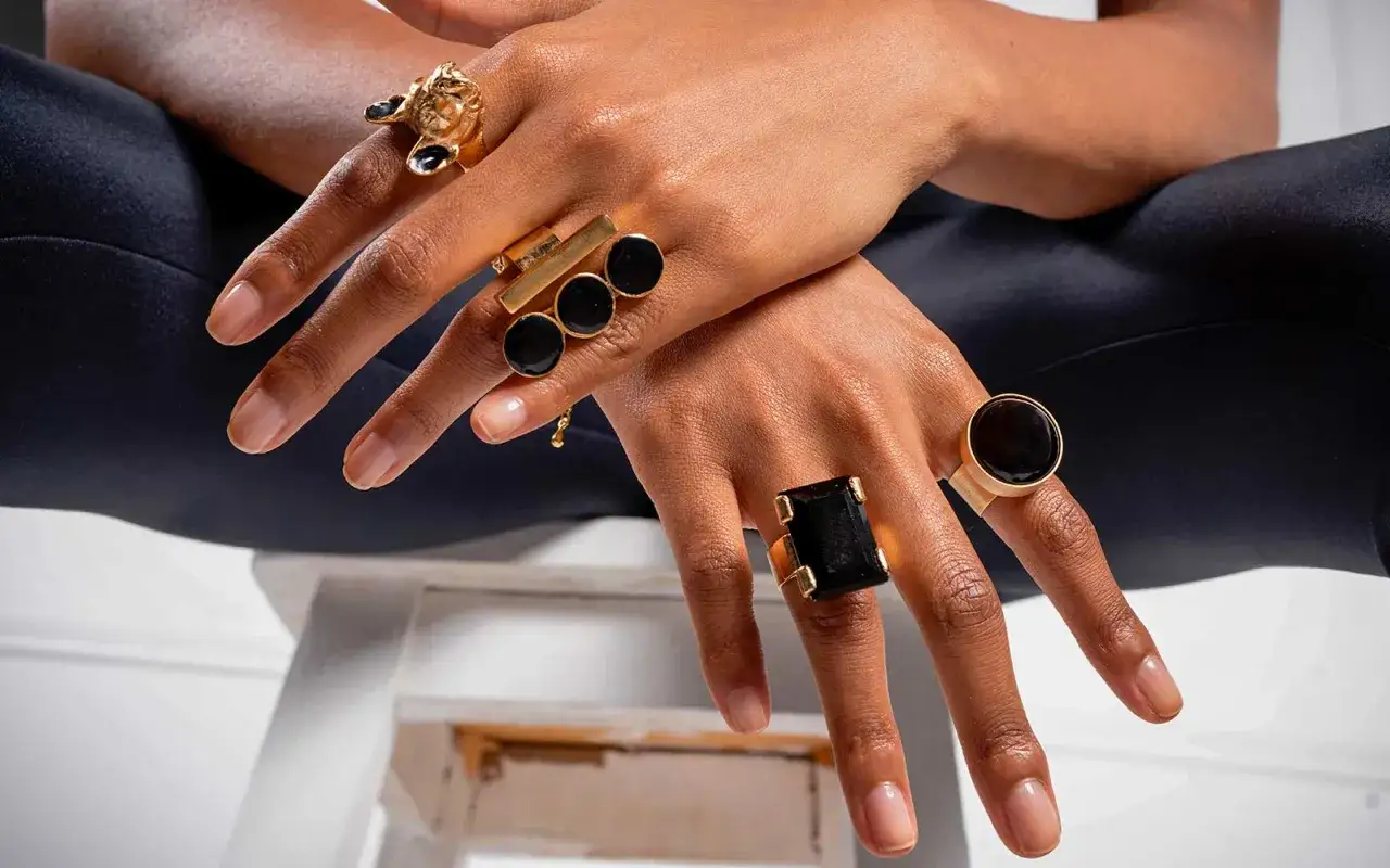 Manos adornadas con llamativos anillos dorados y negros. Un dise&ntilde;o con forma de le&oacute;n, otro con tres c&iacute;rculos negros y un gran anillo rectangular negro.