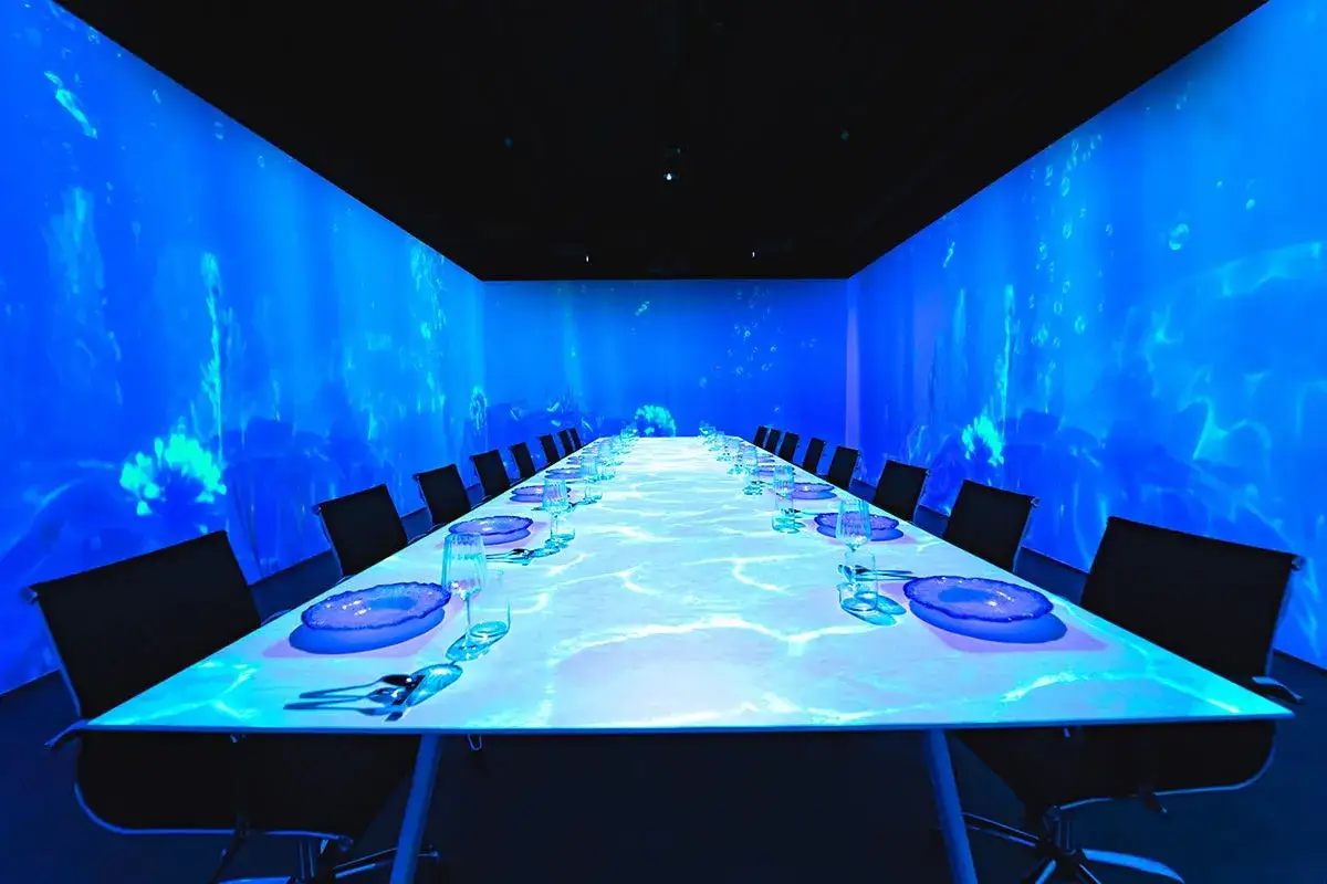 Un restaurante con una experiencia sensorial inmersiva, donde las paredes y la mesa proyectan un mundo submarino azul vibrante.