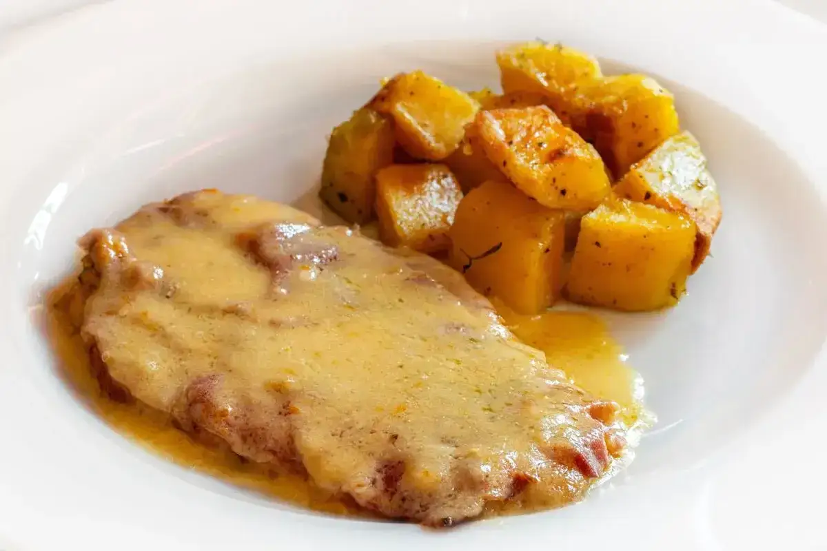 Cotoletta alla bolognese succulenta, ricoperta da una cremosa salsa, accompagnata da patate arrosto speziate.