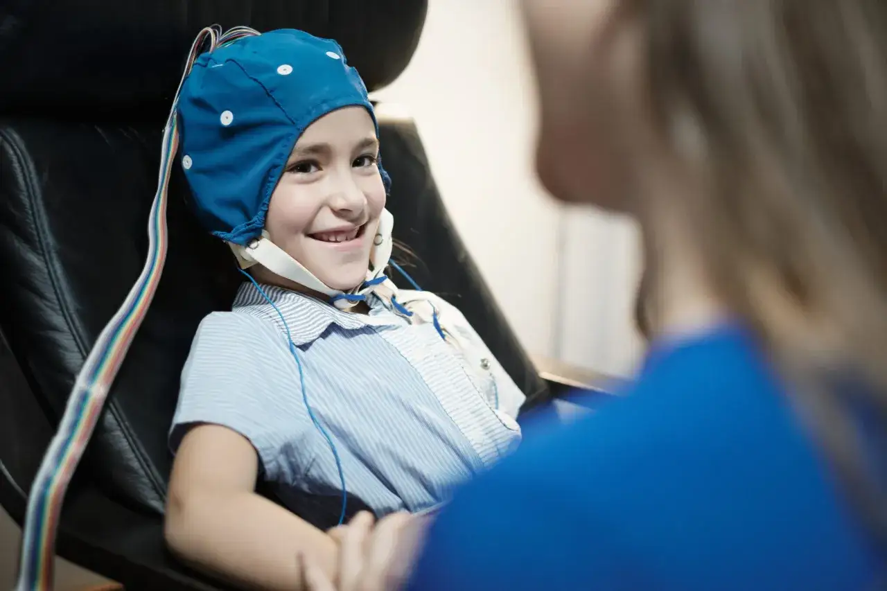 Uśmiechnięta dziewczynka w czepku do EEG, badanie mózgu może pomóc w diagnozie zespołu Aspergera.