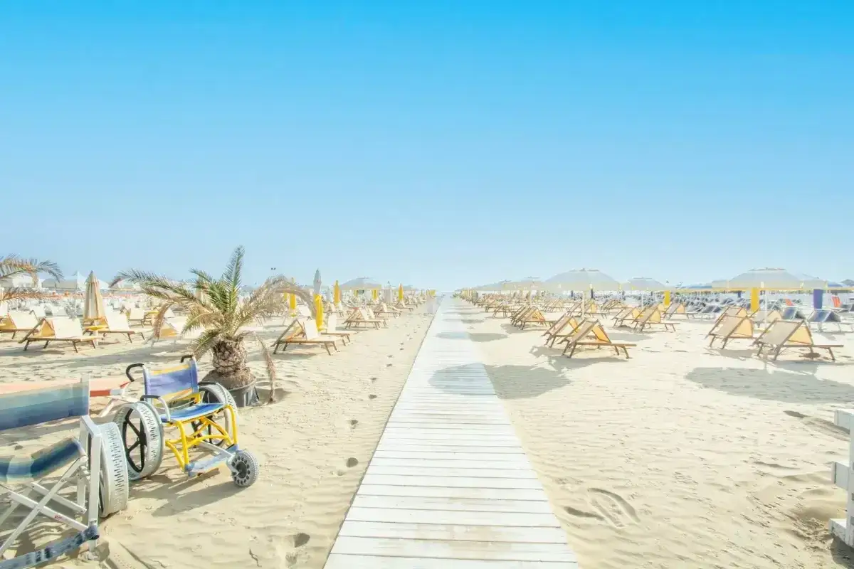 Spiaggia attrezzata a Misano Riccione con passerella, lettini, ombrelloni e una sedia a rotelle speciale per la sabbia.