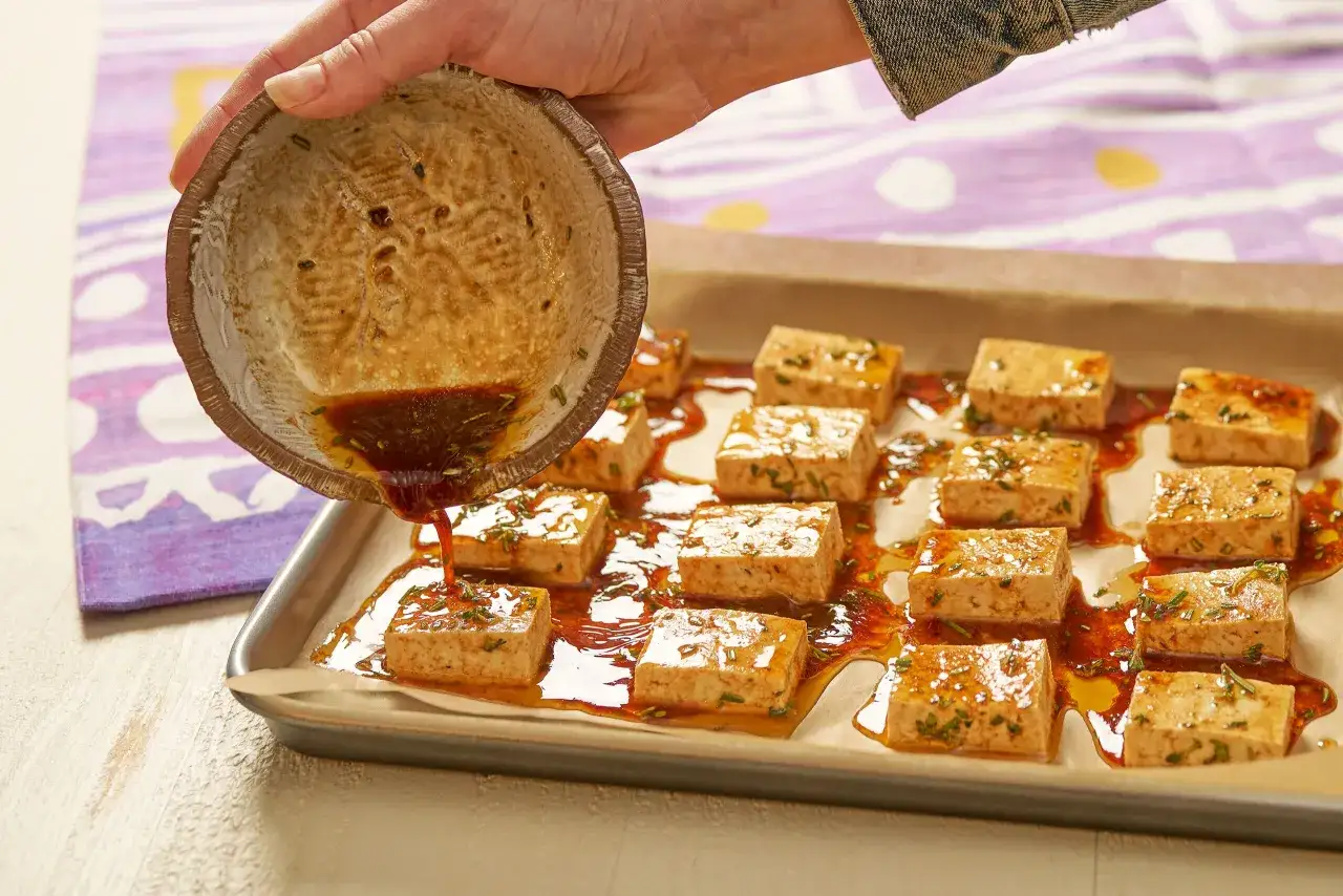Marinade wird &uuml;ber gew&uuml;rfelten Tofu gegossen, der auf einem Backblech liegt. Das Tofu marinieren ist der erste Schritt zu einem k&ouml;stlichen Gericht.