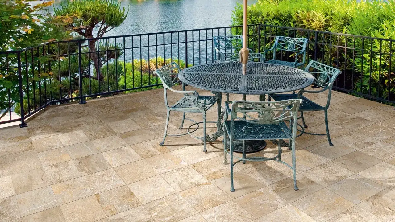 Terrasse avec mobilier de jardin sur un sol en gr&egrave;s c&eacute;rame &eacute;maill&eacute; aux tons sable, surplombant un plan d'eau entour&eacute; de verdure.