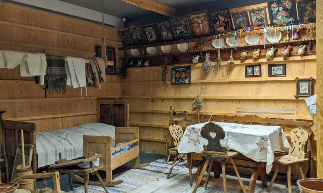 Wnętrze izby w muzeum w Szczawnicy: ł&oacute;żko, kołyska, st&oacute;ł z haftowanym obrusem i tradycyjne ozdoby na ścianach.