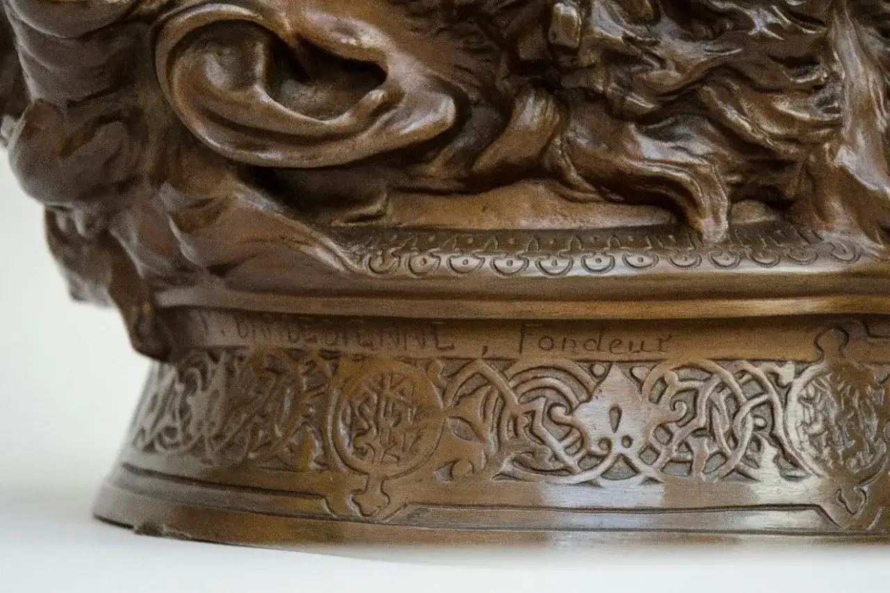 D&eacute;tail d'une sculpture en bronze, creux ou plein, orn&eacute;e de motifs complexes et d'une inscription grav&eacute;e.