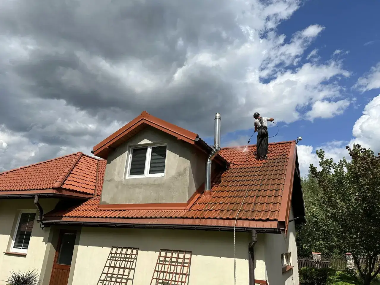 Czyszczenie dachu z mchu. Pracownik myjką ciśnieniową usuwa mech z gontów bitumicznych, przywracając im dawny blask.
