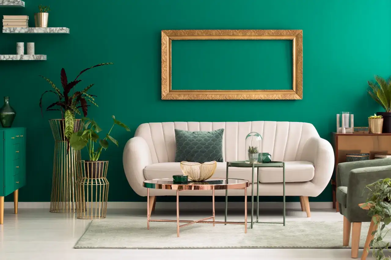 Elegancki salon w butelkowej zieleni. Kremowa sofa, złote dodatki i rośliny tworzą przytulną atmosferę.