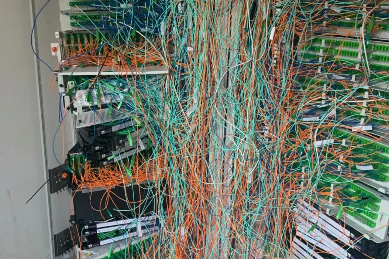 Un enchevêtrement de câbles de fibre optique orange, bleu et vert, connectés à des équipements réseau.