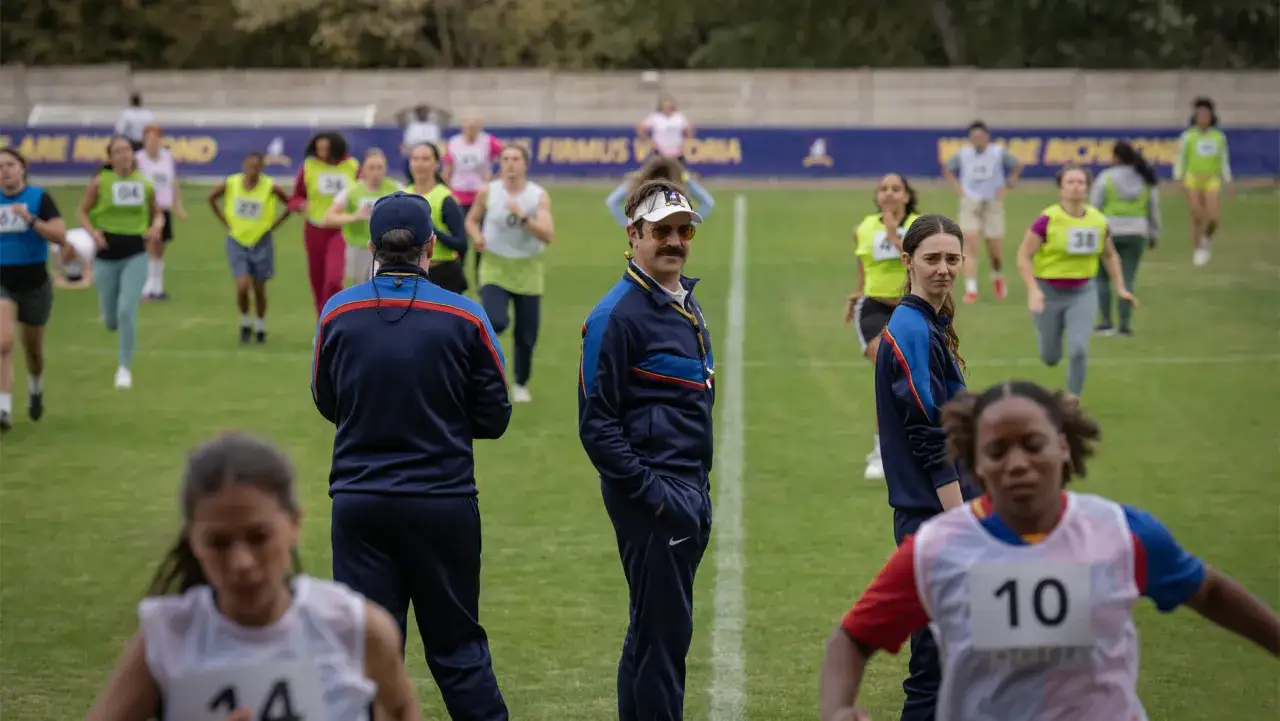 Ted Lasso beobachtet ein Rennen, bei dem Läuferinnen mit Startnummern auf einer grünen Wiese antreten. Vielleicht ein Vorgeschmack auf Ted Lasso Staffel 4?