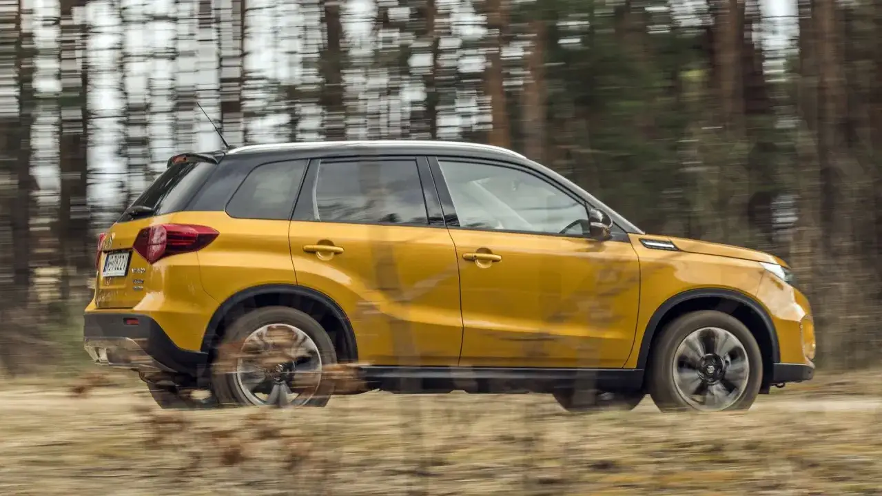 Żółty Suzuki Vitara w ruchu, zamazane tło lasu. Sprawdź suzuki vitara wymiary, by poznać jego kompaktowe gabaryty.