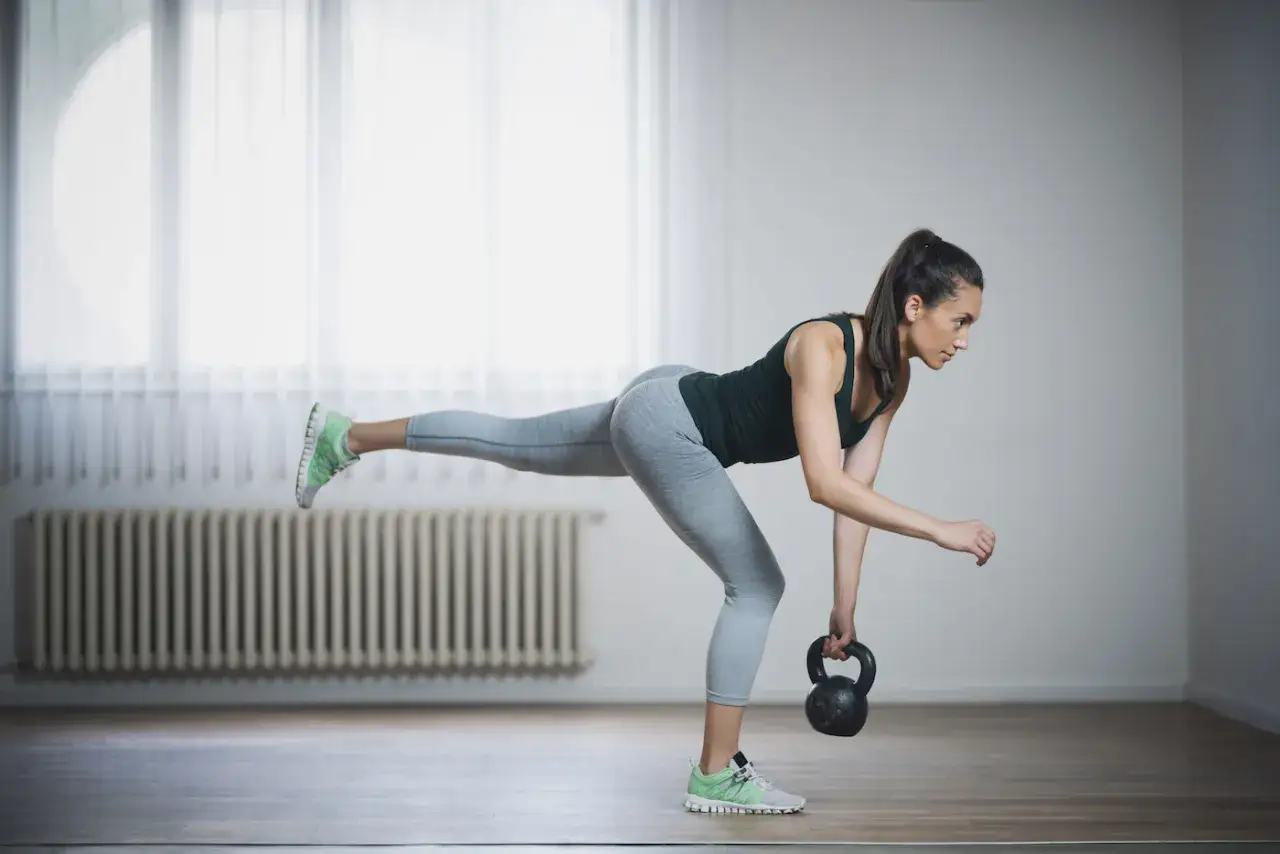 Kvinna utf&ouml;r enbens marklyft med kettlebell. Hon balanserar p&aring; ett ben med det andra rakt bak&aring;t.