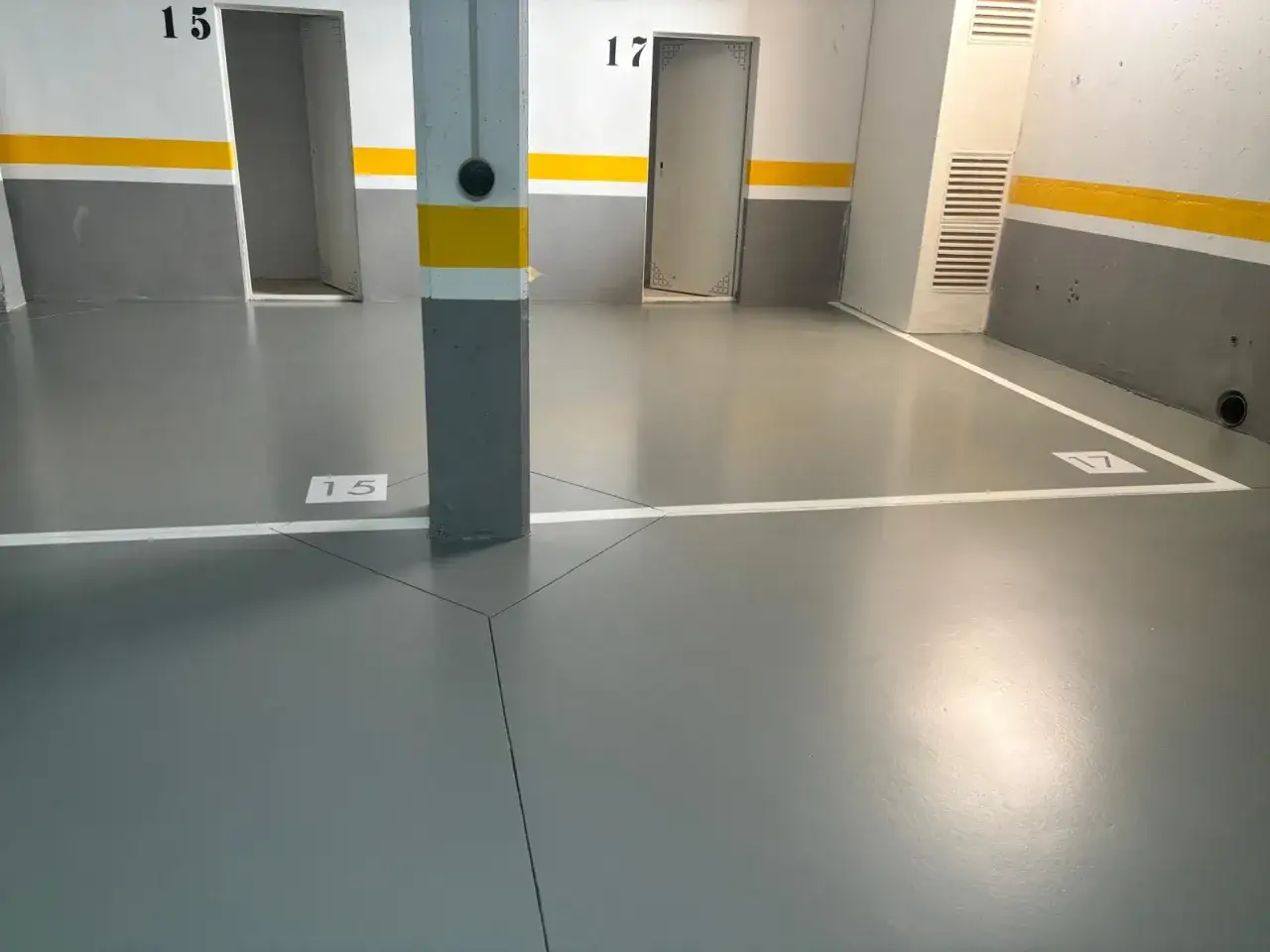 Suelo de garaje con pintura epoxi gris, se&ntilde;alizado con n&uacute;meros 15 y 17, y l&iacute;neas blancas.