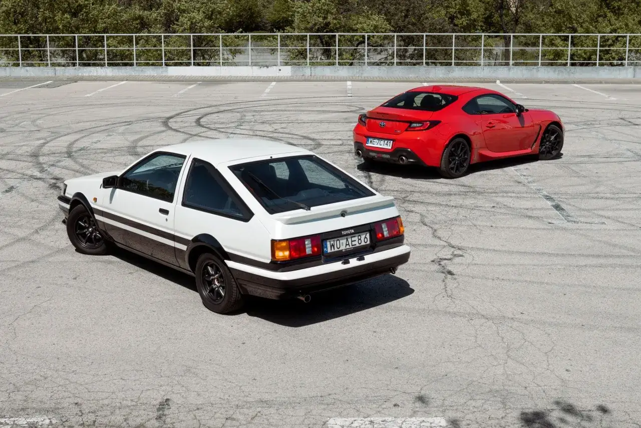 Białe AE86 i czerwona Toyota GR86 na placu z widocznymi śladami opon.