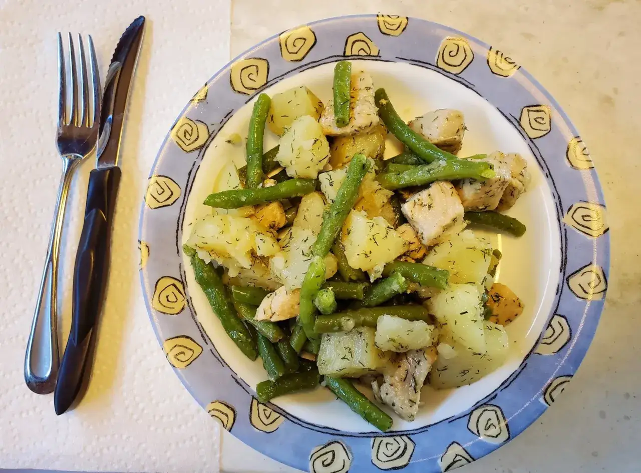 En tallrik med fransk potatissallad med kyckling, gr&ouml;na b&ouml;nor och dill. En kniv och gaffel ligger bredvid.