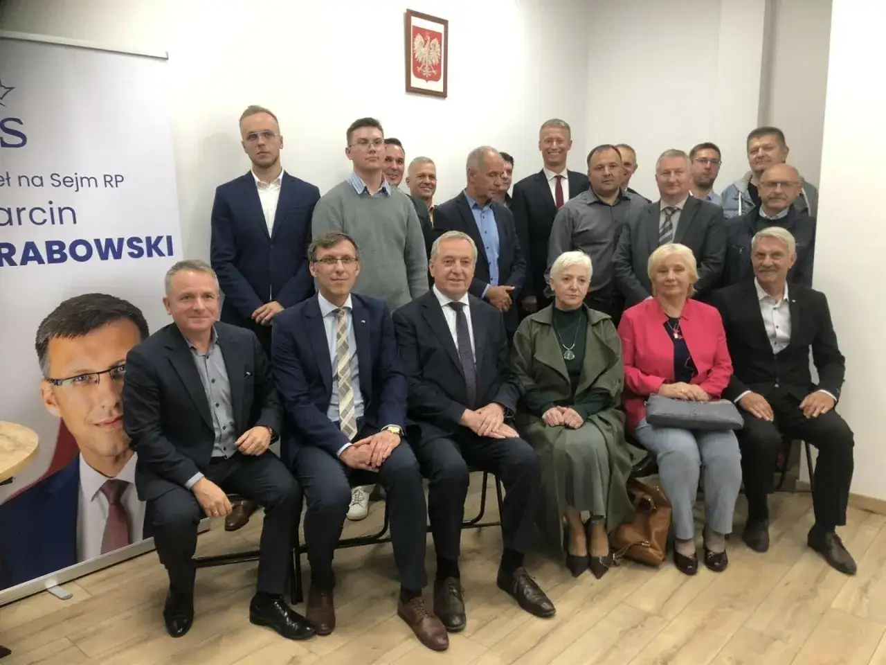 Grupa osób pozuje do zdjęcia w biurze poselskim PiS w Warszawie. W tle plakat wyborczy Marcina Rabowskiego.