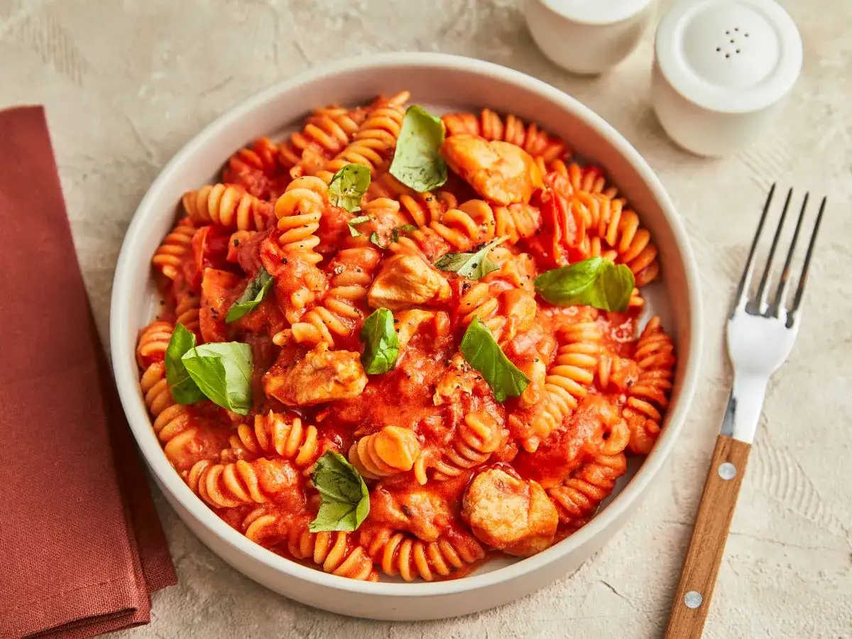 Makaron fusilli z kurczakiem w sosie pomidorowym, udekorowany bazylią. Idealne danie, co można ugotować na szybko.