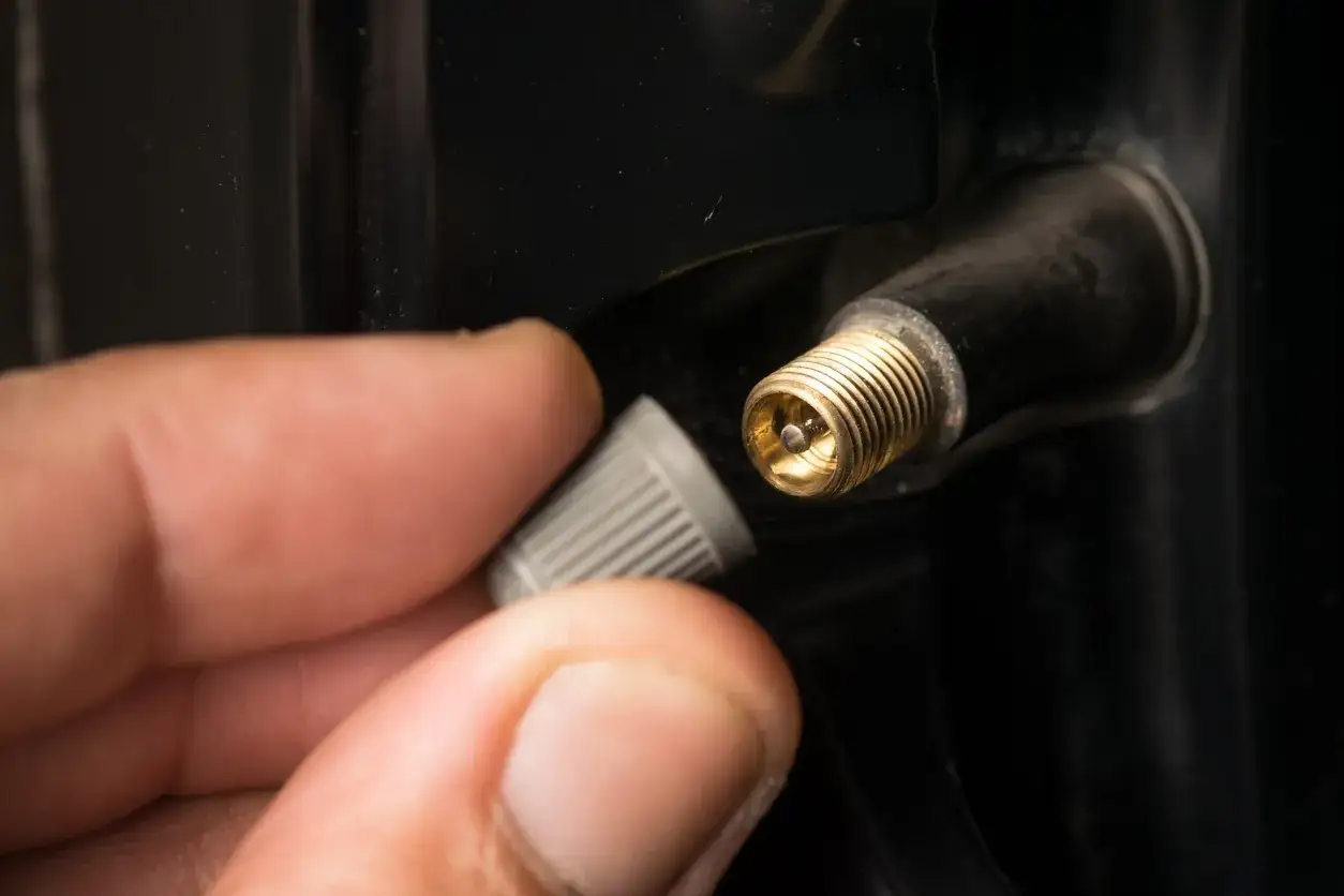 Main d'une personne retirant le capuchon d'un valve pneu qui fuit, révélant le mécanisme interne.