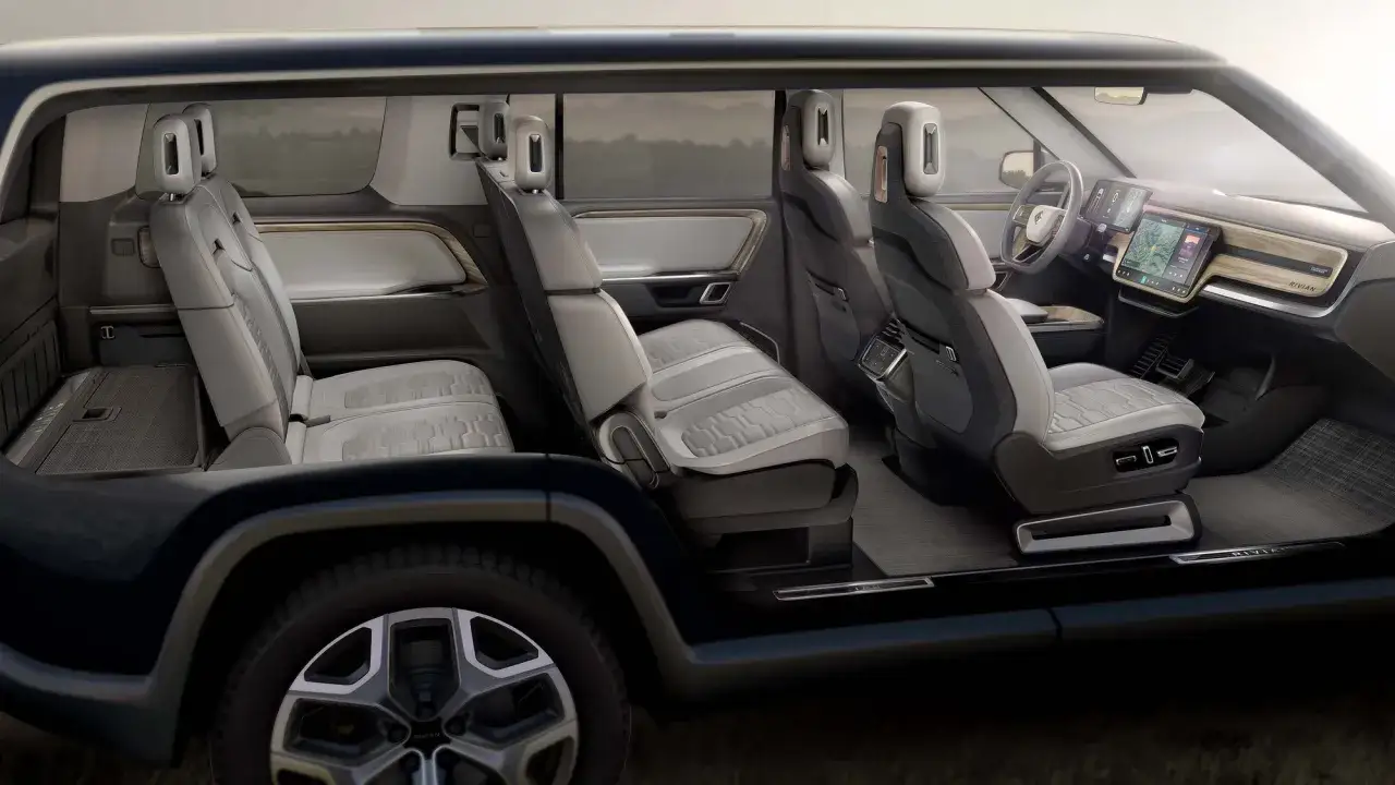 Interior de coches el&eacute;ctricos grandes con asientos de cuero gris y detalles de madera. Pantalla t&aacute;ctil central y tablero moderno.