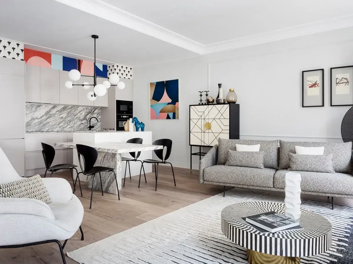 Un loft peque&ntilde;o moderno con cocina integrada, mesa de m&aacute;rmol, sof&aacute; gris y mesa de centro geom&eacute;trica.