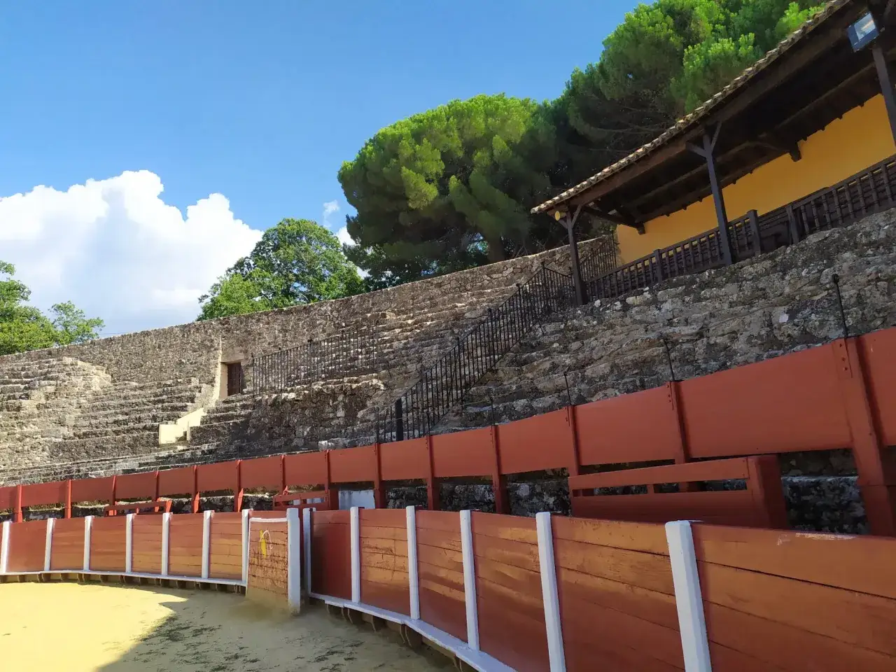 Arena de la primera plaza de toros de España, con gradas de piedra y barreras de madera bajo un cielo azul.