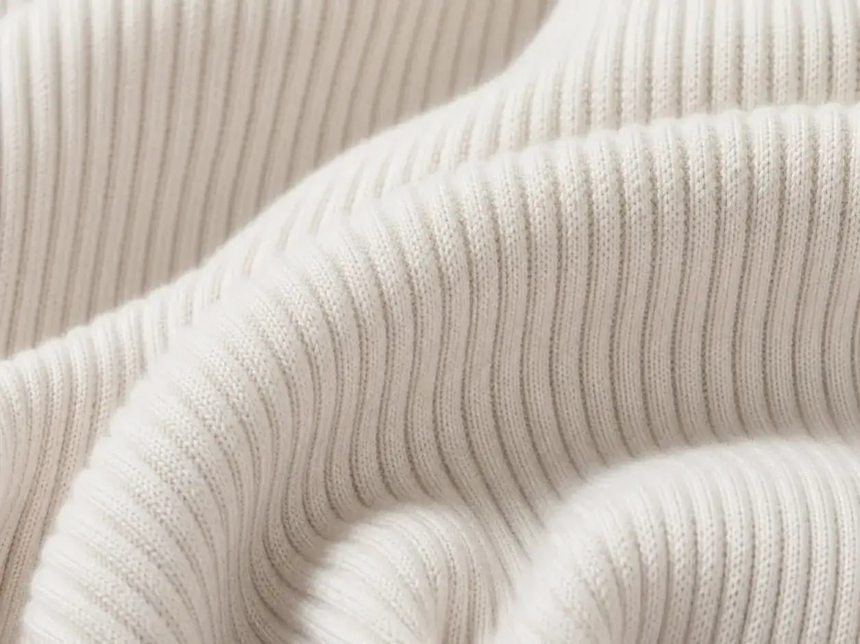 Close-up of soft, cream-colored fabric with a ribbed texture. Ribbed means it has raised parallel cords or ridges, giving it a distinctive look and feel.