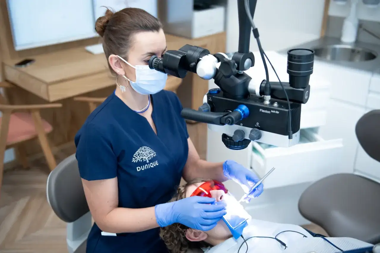 Dentystka pod mikroskopem, badając ząb pacjenta. To przykład precyzyjnej stomatologii, gdzie nawet skomplikowane zabiegi, jak kortykotomia, są wykonywane z najwyższą dokładnością.