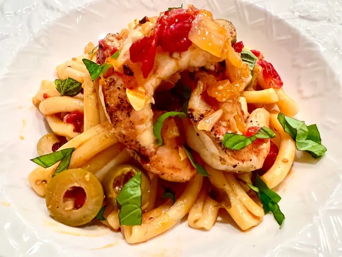 Spaghetti mit Garnelen mediterran, garniert mit frischem Basilikum und grünen Oliven. Ein köstliches Gericht, das nach Sommer schmeckt.