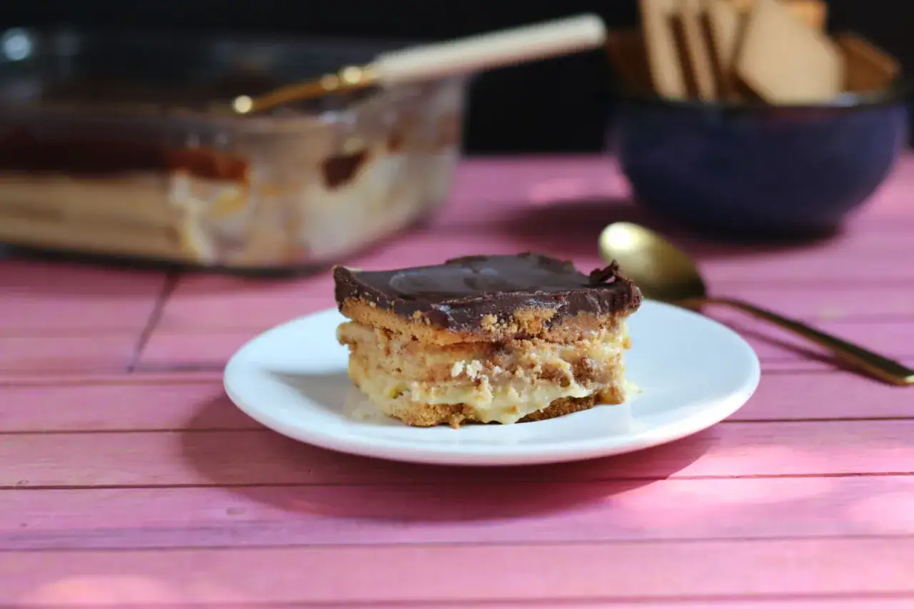 Ein St&uuml;ck spanischer Kuchen mit Schokoladenglasur und cremiger F&uuml;llung auf einem Teller.